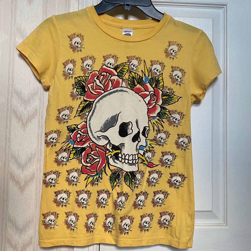 Yellow Ed Hardy short-sleeve top printed with a large skull and red roses over a repeating skull pattern, shown on a hanger